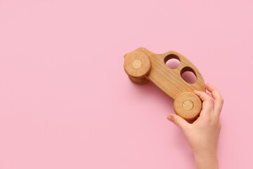 Child's hand with wooden toy car on pink background, closeup