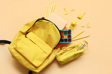 School backpack with different stationery supplies on beige background
