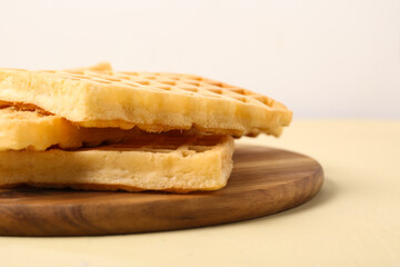Wooden board with tasty Belgian waffles on yellow table