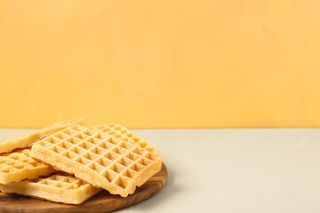 Wooden board with tasty Belgian waffles on yellow background