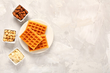 Plate with tasty Belgian waffles and bowls of different nuts on grey background