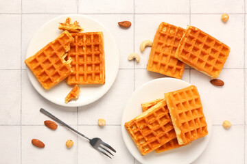 Plates with tasty Belgian waffles and different nuts on white tile background
