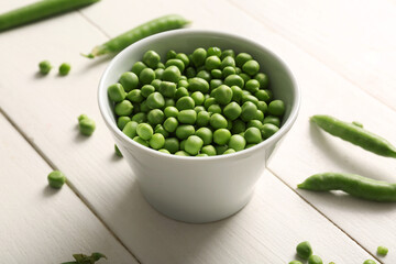 Bowl of green peas on white wooden background