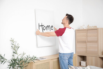 Young man hanging poster on light wall at home