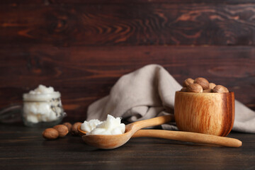 Spoons with shea butter and nuts on wooden background