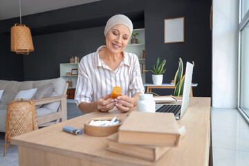 Mature woman after chemotherapy with bottle of weed sitting near table at home
