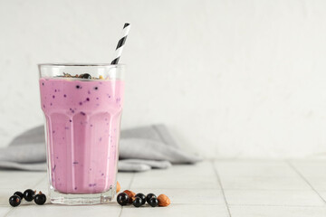Glass of fresh smoothie with black currant on white tile table