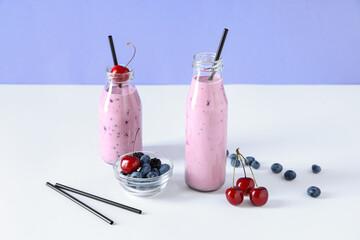 Bottles of fresh smoothie with blueberries, blackberries and cherries on blue background