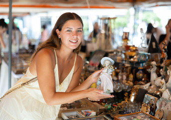 Smiling female tourist looking at various vintage items at street flea market