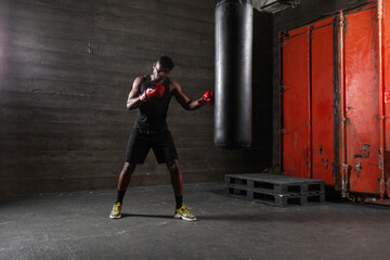 Powerful African American boxer wearing red gloves prepares to hit punching bag in gym showing his...