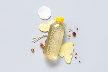 Bottle of micellar water, pieces of apple, nuts and cotton pad on grey background