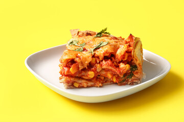 Plate with piece of tasty enchilada on yellow background