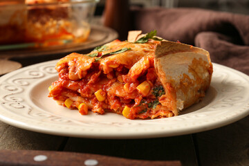Plate with piece of tasty enchilada on wooden table, closeup