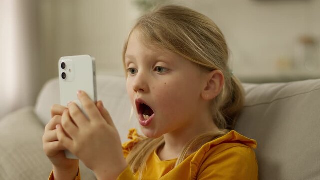 Little European girl holding mobile phone smartphone cellphone surprised wow shocked unexpected emotional amaze victory technology gadget web network excited child kid pupil daughter delight astonish