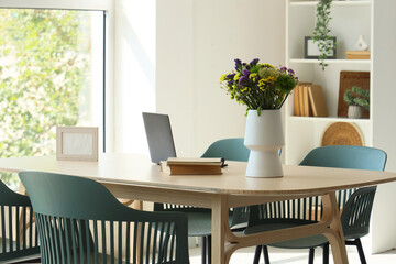 Vase with wildflowers, books and laptop on dining table in room