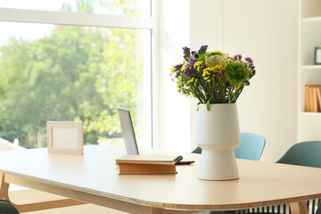 Vase with wildflowers, books and laptop on dining table in room