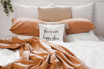 Big comfortable bed with crumpled linen and pillow with text THIS IS OUR HAPPY PLACE in room. Closeup