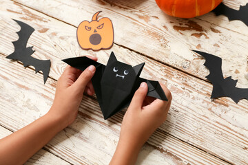 Child making Halloween decorations and origami bat on wooden background