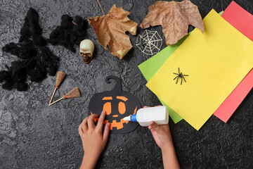 Child with glue making Halloween decorations on grunge black background