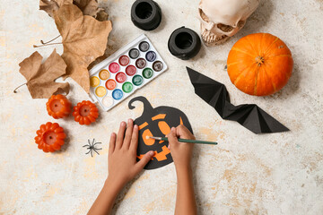 Child with supplies and decorations painting Halloween pumpkin on grunge white background