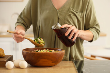 Young woman pouring kvass into okroshka in kitchen, closeup