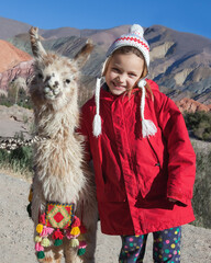 smiling girl with alpaca with a desert hills landscape in the background © atikinka2