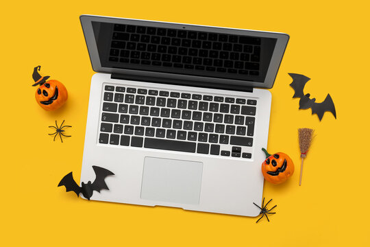 Composition with modern laptop and decor for Halloween on yellow background