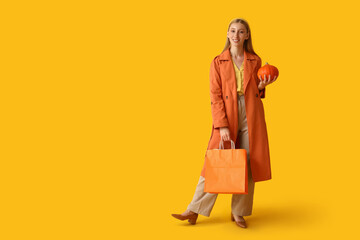 Young woman in autumn clothes with shopping bags on yellow background