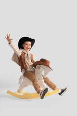 Cute little cowboy on rocking horse against light background
