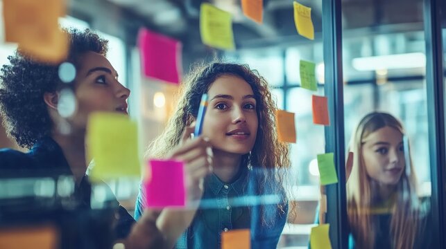 A group of colleagues brainstorming with sticky notes on a glass wall in a creative office setting