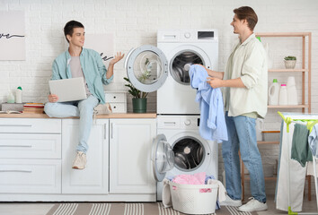 Male students with laptop doing laundry in dormitory