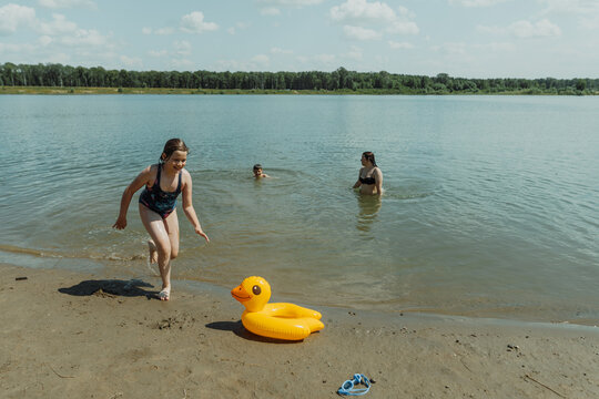Happy family playing at the lake with inflatable duck float. They are enjoying a beautiful summer day by the water with an inflatable yellow duck float - Powered by Adobe