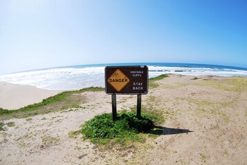 Danger sign warns of unstable cliffs on ocean beach