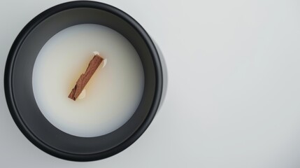Wooden wick floating in scented candle wax inside a black container on white surface