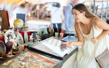 Girl in flea market store look at silver cutlery, antique gifts. Surprised girl points finger at...