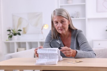 Senior woman with magnifying glass reading medicine instruction at table indoors