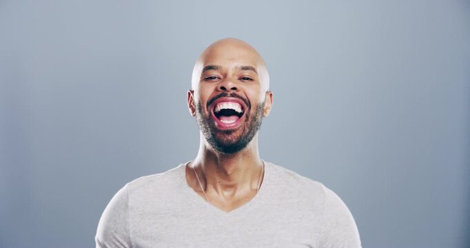 Comic, face and man laughing in a studio for funny or silly joke in conversation with happiness. Smile, portrait and young male model from Colombia with goofy facial expression by gray background.