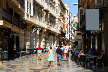 Obraz premium Typical vibrant narrow pedestrian street of Cartagena city with picturesque architecture and outdoor cafes on sunny summer day, Spain