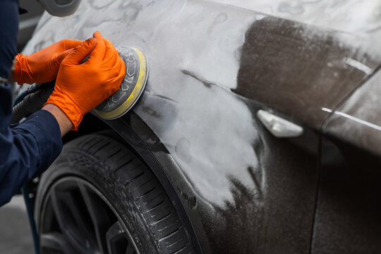 A mechanic sands the putty on a car body with a machine. Repair after an accident. 