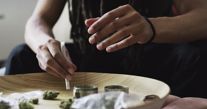 Man, marijuana and rolling cigarette in home, 420 and cannabis preparation at table. African person with weed joint, hands on drugs abuse and hemp paper, natural cbd plant or thc addiction in house