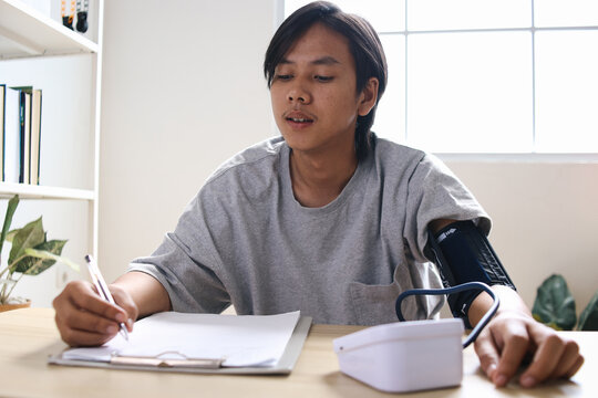 Young Asian Male Medical Checking At Home Using Blood Pressure Test