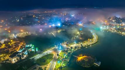 Aerial view of a Da Lat City in the mist magical night, hiden in the fog and clouds. Urban development texture, transport infrastructure. Tourist city in developed Vietnam. Night cityscape