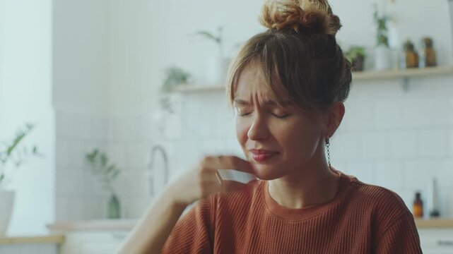 Young feverish woman touching her neck and forehead, suffering from sore throat and headache at home