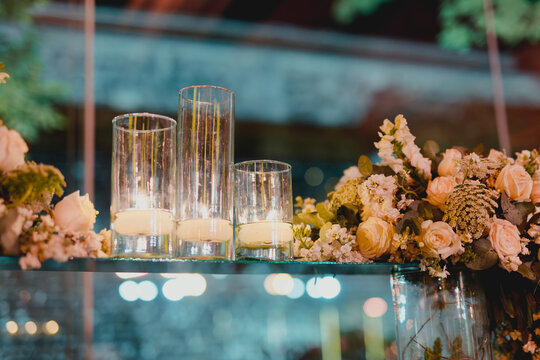 Elegant white candles in clear glass vases decorating a luxury wedding centerpiece at a nighttime reception. Romantic candlelight creates a warm and sophisticated atmosphere for an outdoor wedding cel
