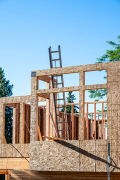 Summer construction season, new house build at the framing stage, aluminum extension ladder on 2nd floor leaning against exterior wall, early morning sunny day
