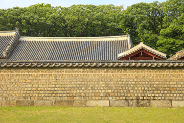 Jongno-gu, Seoul, South Korea - May 20, 2022: Front view of stonewall with tile roof against tile house and trees at Jongmyo Shrine