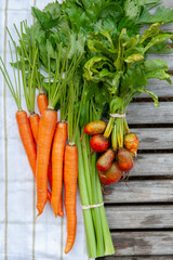 bunches of market fresh vegetables laying on a towel on wood.