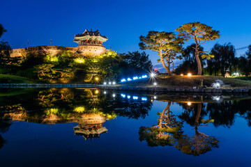 Paldal-gu, Suwon-si, Gyeonggi-do, South Korea - August 18, 2019: Night view of Yongyeon Lake and pine trees with reflection on water against Banghwasuryujeong Pavilion of Suwon Hwaseong Fortress