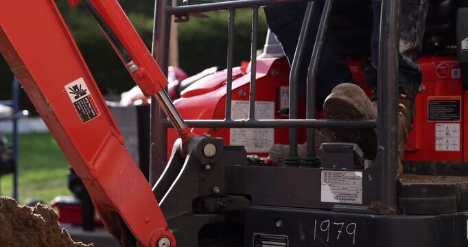 Construction worker operating mini excavator - close up on feet and pedals and bucket