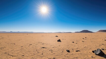 Wide expanse of desert with a few scattered rocks, under a clear, deep blue sky, the sun high above